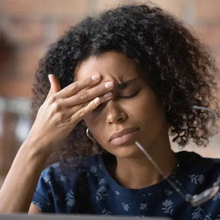 A person touches the side of the head at a desk, suggesting concentrated focus amid a softly lit indoor setting